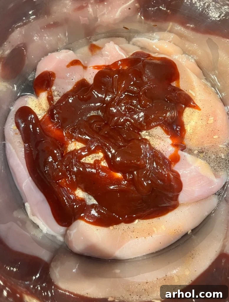 Chicken breasts layered with seasoning and Sweet Baby Ray's BBQ sauce inside an Instant Pot electric pressure cooker, ready to be cooked