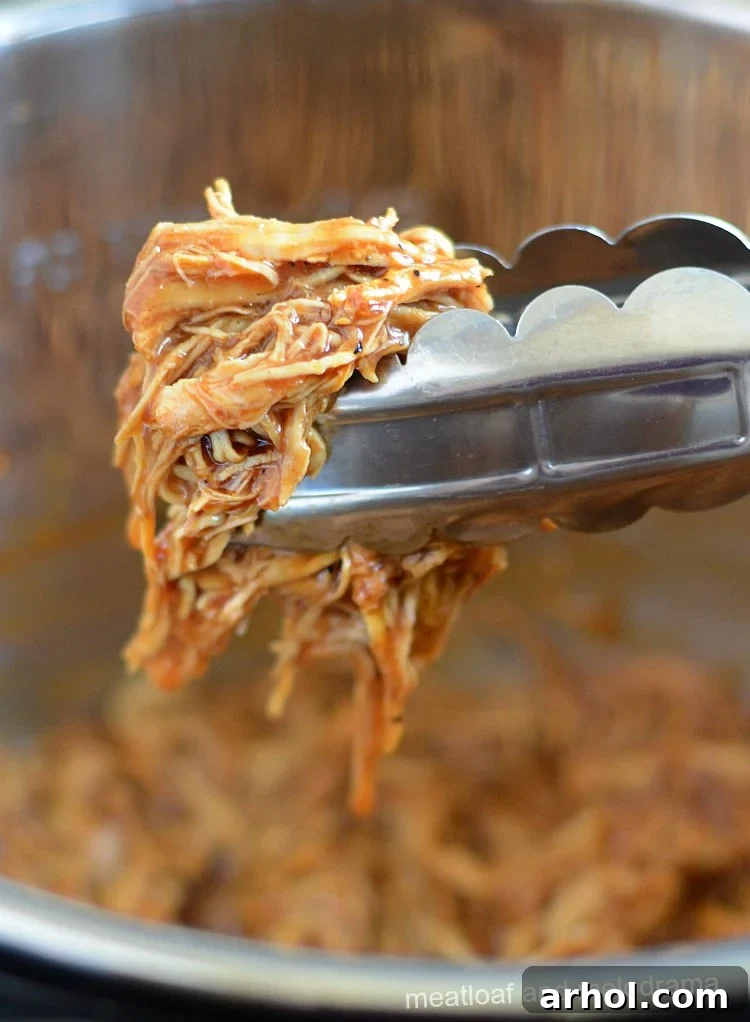 Tender Instant Pot BBQ pulled chicken held in metal tongs, showing its shredded texture