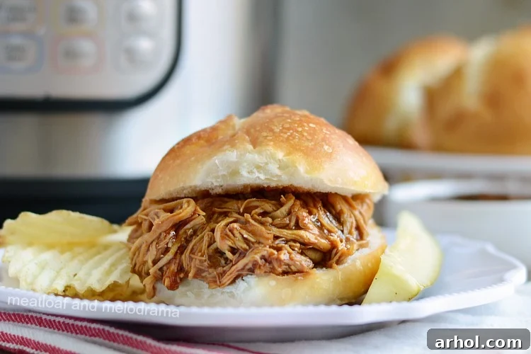 A delicious Instant Pot BBQ chicken sandwich with a pickle on a plate, ready to be eaten