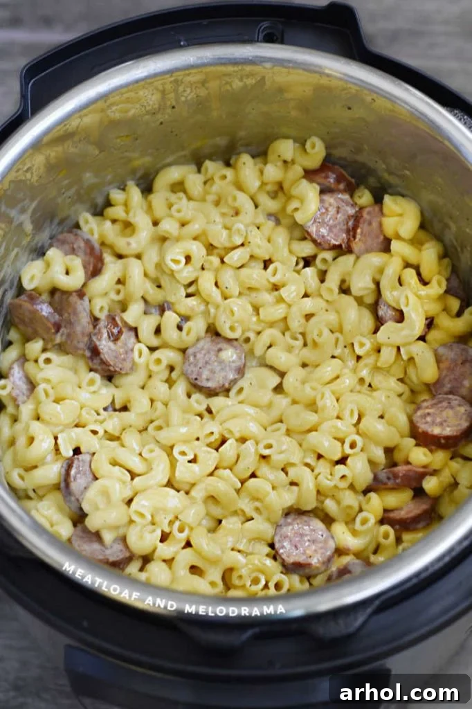 Creamy mac and cheese with kielbasa slices being stirred inside the Instant Pot after the pressure cooking phase.