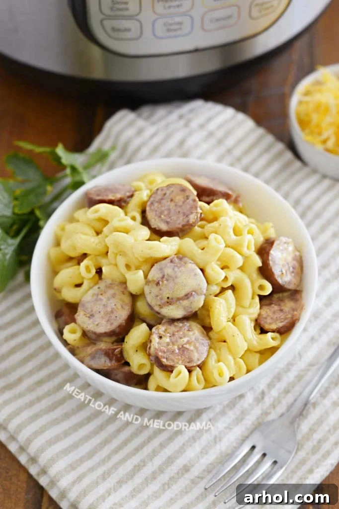Close-up view of a bowl of creamy mac and cheese generously topped with sliced smoked sausage.