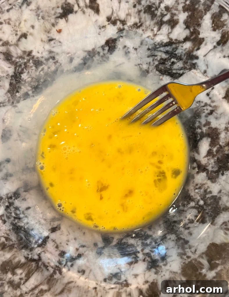 Lightly beaten eggs in a mixing bowl with a fork, ready for the next ingredients.