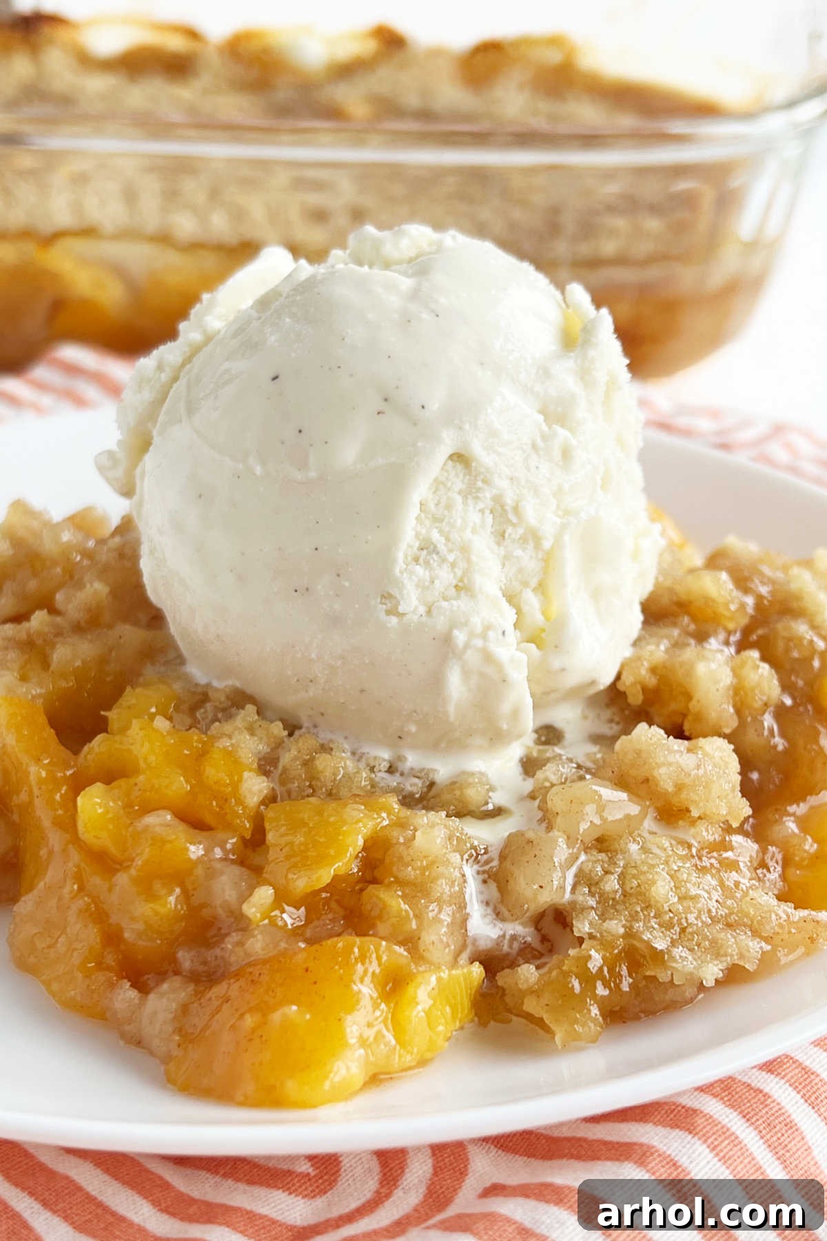 Summertime Peach Crisp Delight 2 Fresh peach crisp with a scoop of vanilla ice cream on a white plate, showcasing the golden-brown topping and juicy peach filling.
