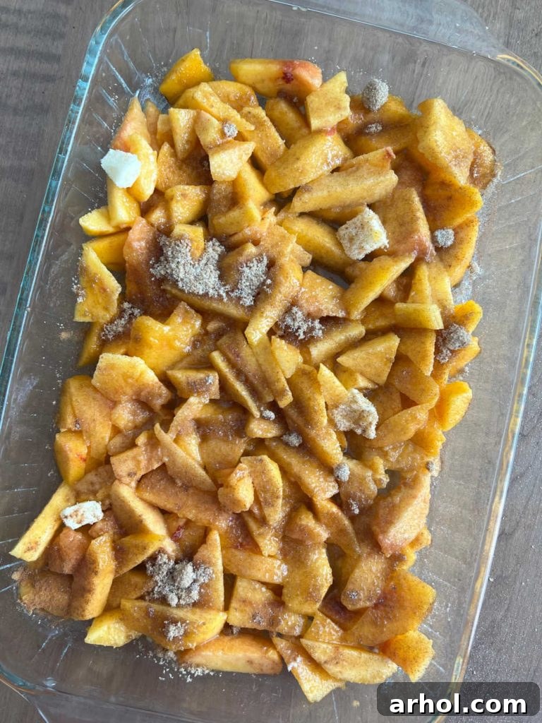 Summertime Peach Crisp Delight 5 Sliced fresh peaches layered in a baking dish, seasoned with sugar and cinnamon, and dotted with butter, ready for the crisp topping.