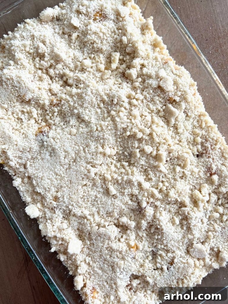 Summertime Peach Crisp Delight 6 Evenly sprinkling the crumb topping over the sliced peaches in a baking dish before baking, ensuring complete coverage.
