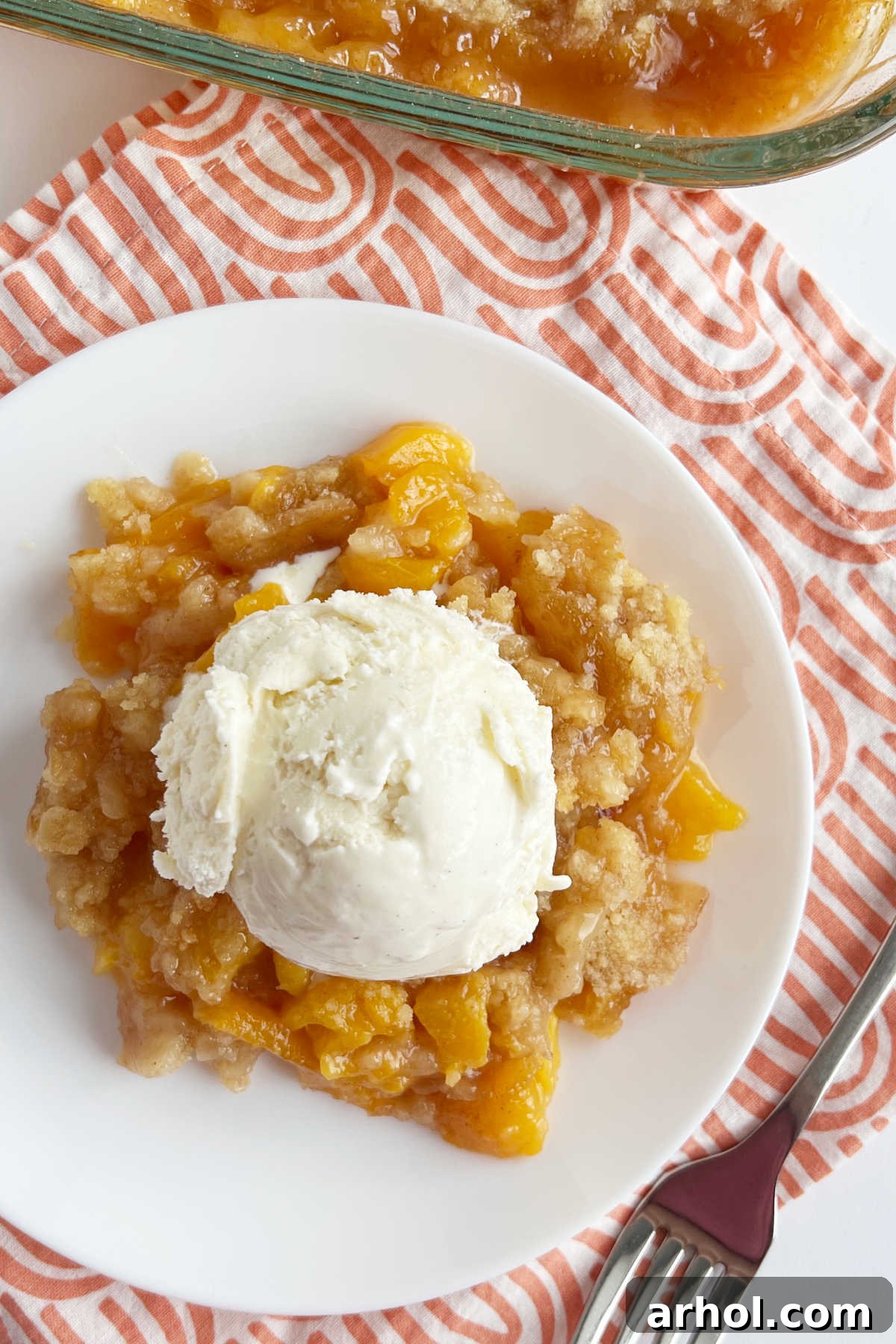 Summertime Peach Crisp Delight 7 A generous serving of fresh peach crisp without oats, topped with a melting scoop of vanilla ice cream, on a white plate, ready to be enjoyed.