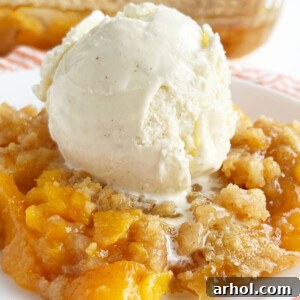 Fresh peach crisp without oats, topped with a scoop of vanilla ice cream, in a white dish.