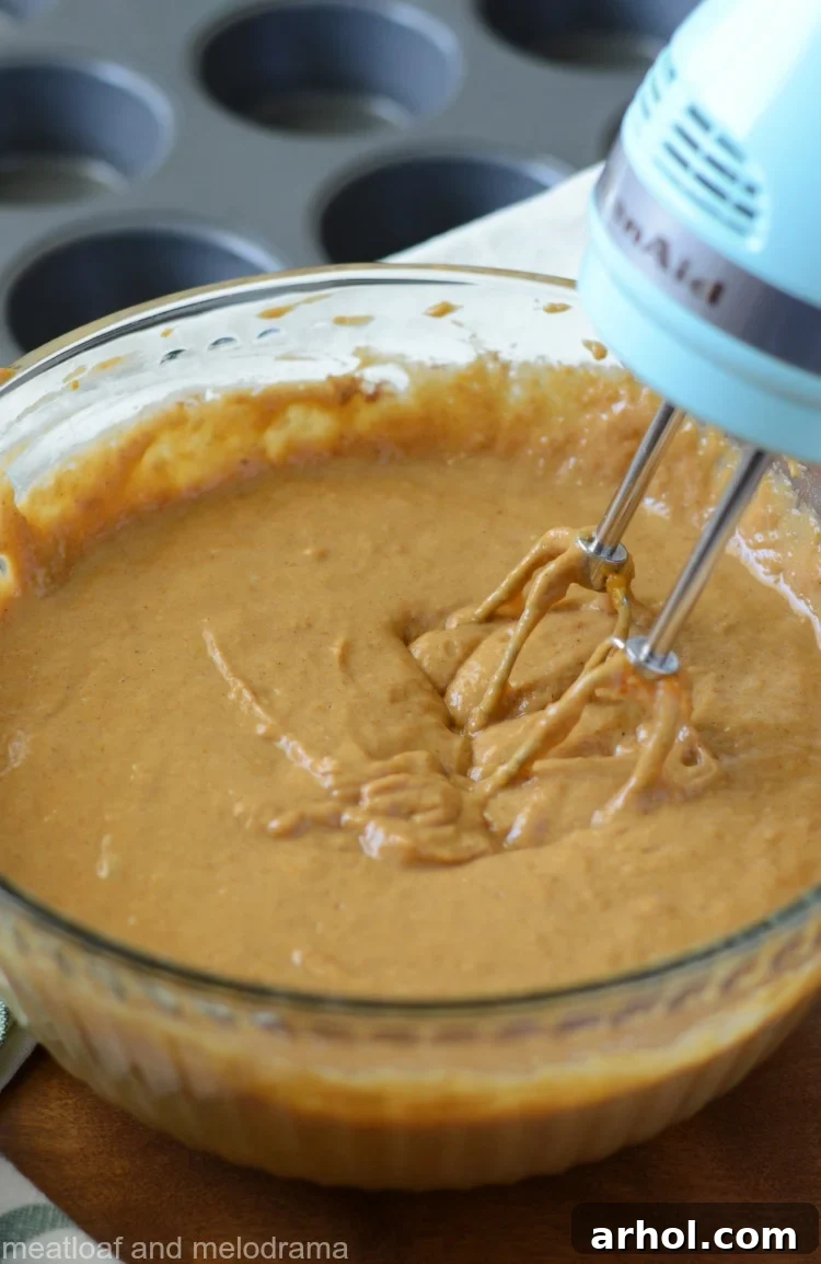 Mixing pumpkin muffin batter in a large mixing bowl with a hand mixer, showcasing the one-bowl method convenience.