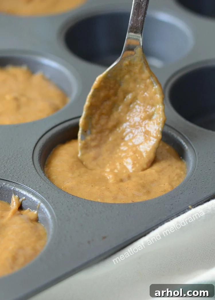 Filling a muffin tin with pumpkin muffin batter, aiming for full cups to achieve tall, fluffy muffins.