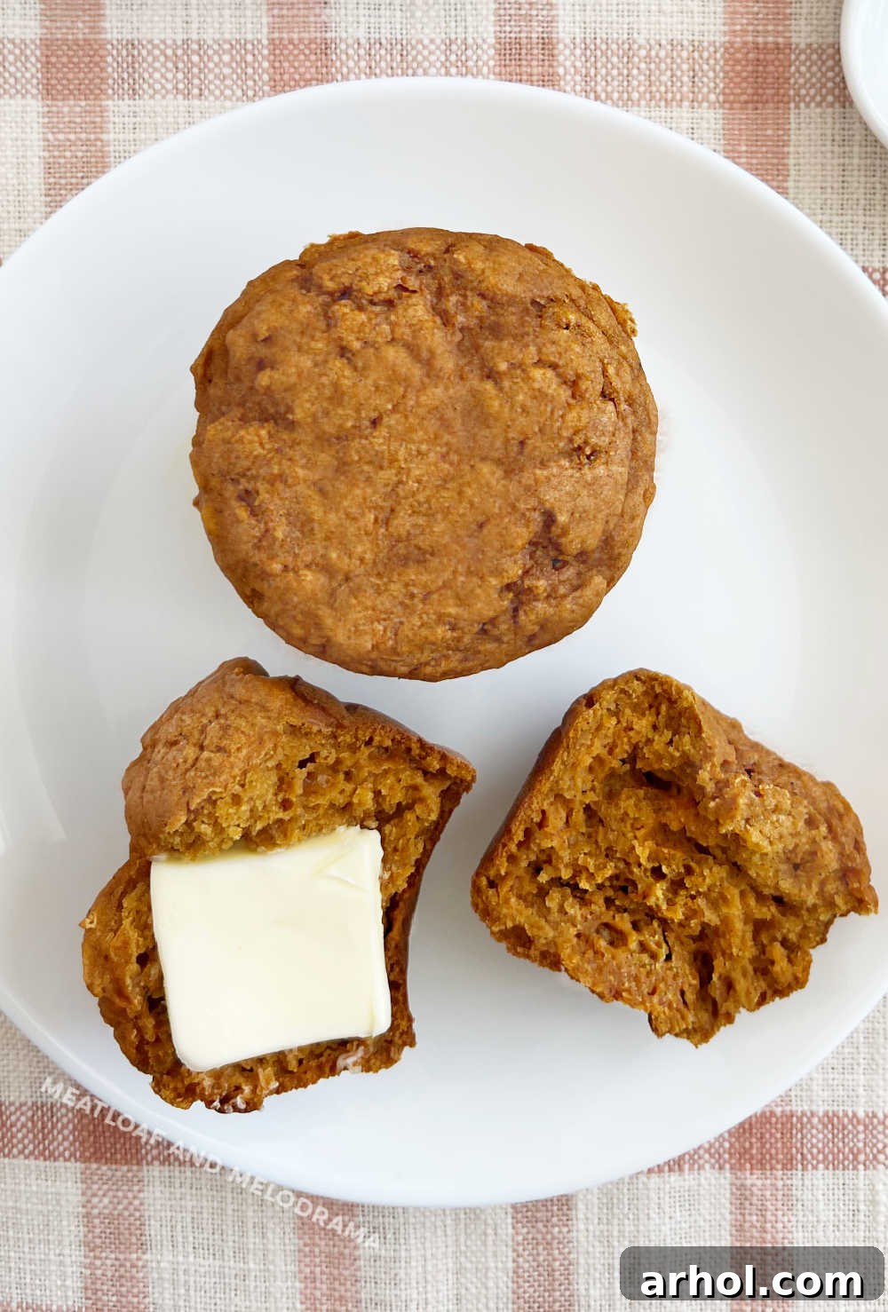 Close-up of a healthy pumpkin applesauce muffin on a plate with a dollop of butter, ready to be enjoyed.