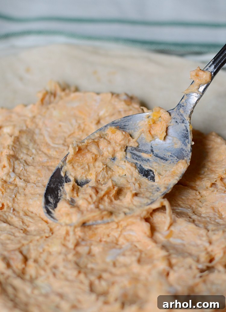 Spreading a creamy Buffalo chicken and cream cheese mixture evenly over a large flour tortilla for roll-ups.