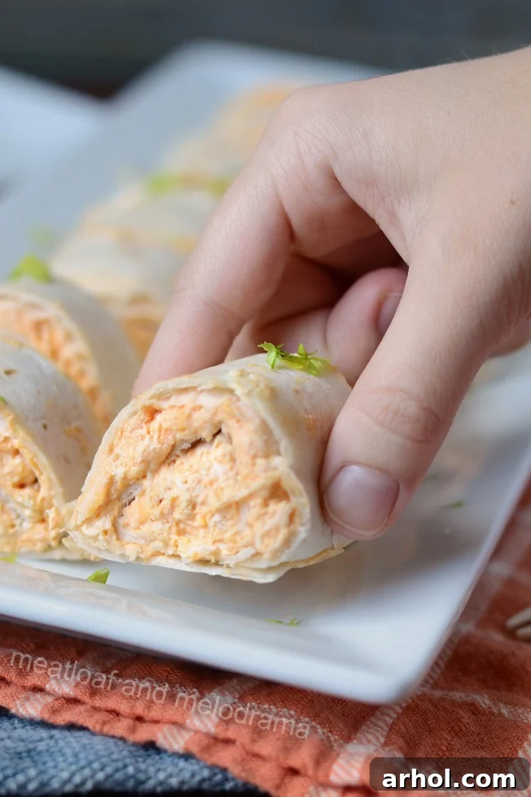 A hand holding a perfectly sliced Instant Pot Buffalo chicken roll-up, showcasing the creamy filling.
