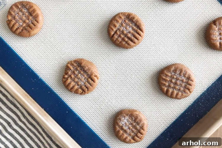 The Easiest 4 Ingredient Peanut Butter Cookies 5 Rows of unbaked peanut butter cookies, each with a distinct criss-cross fork pattern, resting on a baking sheet.