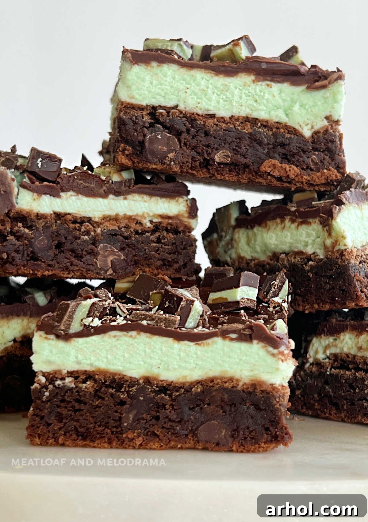 Mint chocolate chip brownies with mint frosting and chocolate ganache, topped with Andes mints, stacked appealingly.