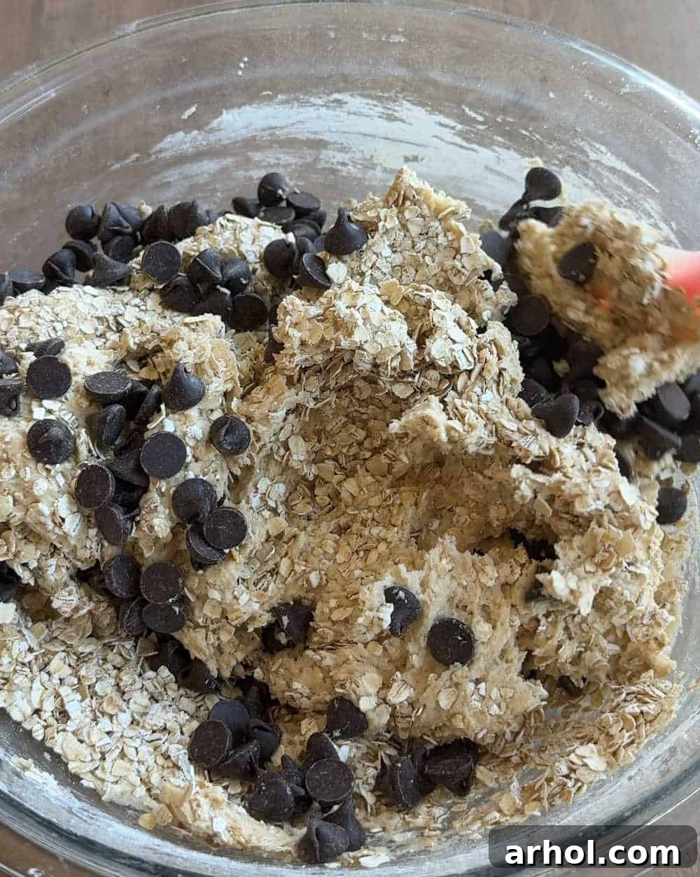 Folding in oats and chocolate chips into cookie dough with a rubber spatula.