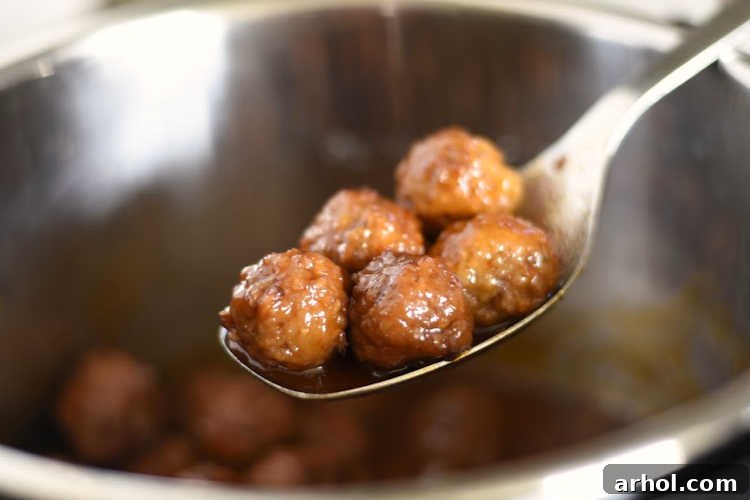 A single grape jelly meatball expertly placed on a serving spoon, showcasing its glistening sauce