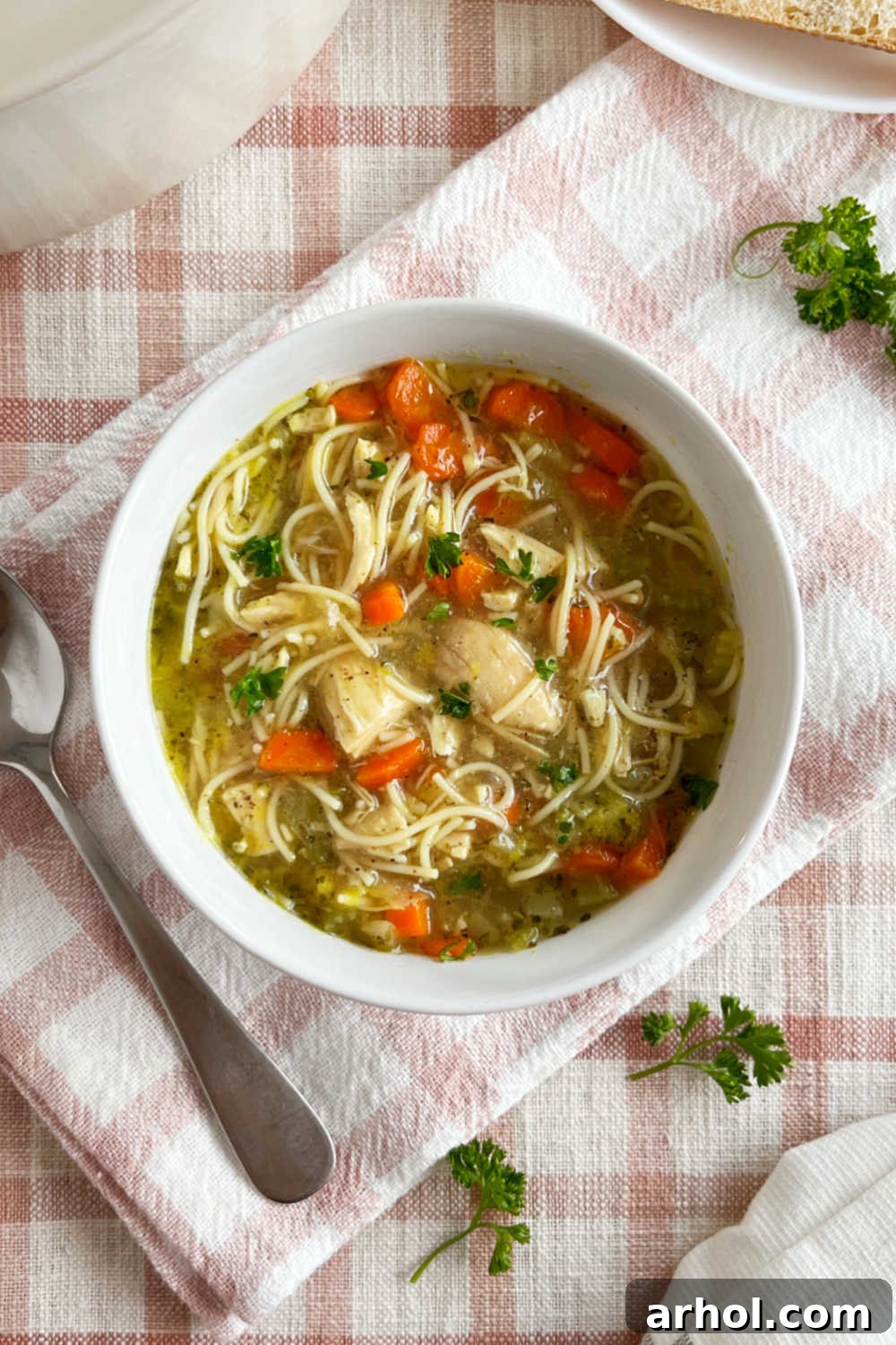 A steaming bowl of homemade chicken noodle soup, garnished with fresh parsley and slices of carrot, on a rustic wooden table, ready to be enjoyed.