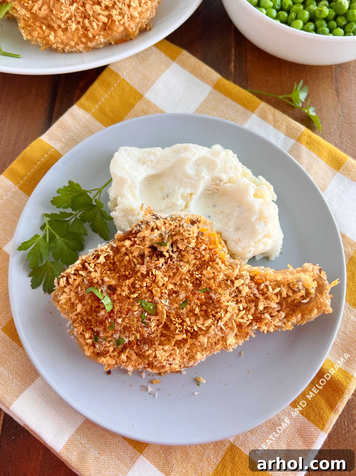 bone-in baked breaded pork chops on the table with mashed potatoes and peas