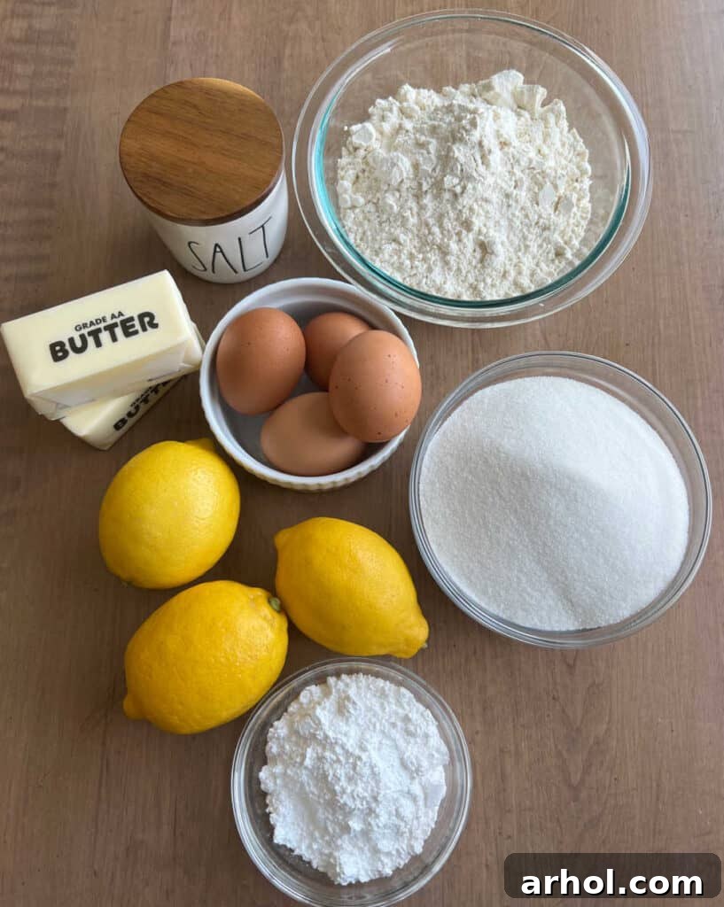 A flat lay photograph displaying all the fresh ingredients needed for lemon bars: whole lemons, eggs, sticks of butter, granulated sugar, powdered sugar, flour, and a pinch of salt.