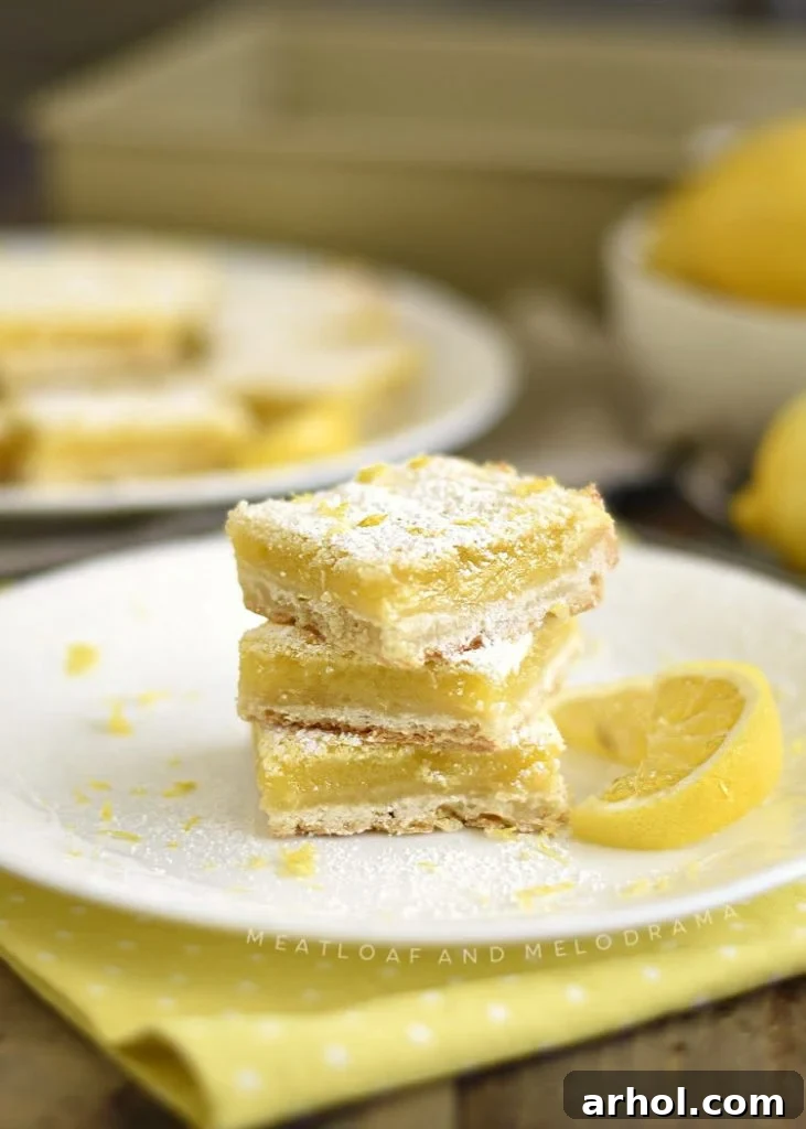 Stack of perfectly cut, easy lemon bars with powdered sugar dusting, arranged on a white ceramic plate, ready for serving.