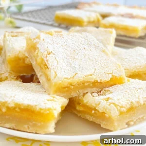 A close-up shot of a single serving of lemon bars with a shortbread crust on a white plate, dusted with powdered sugar.