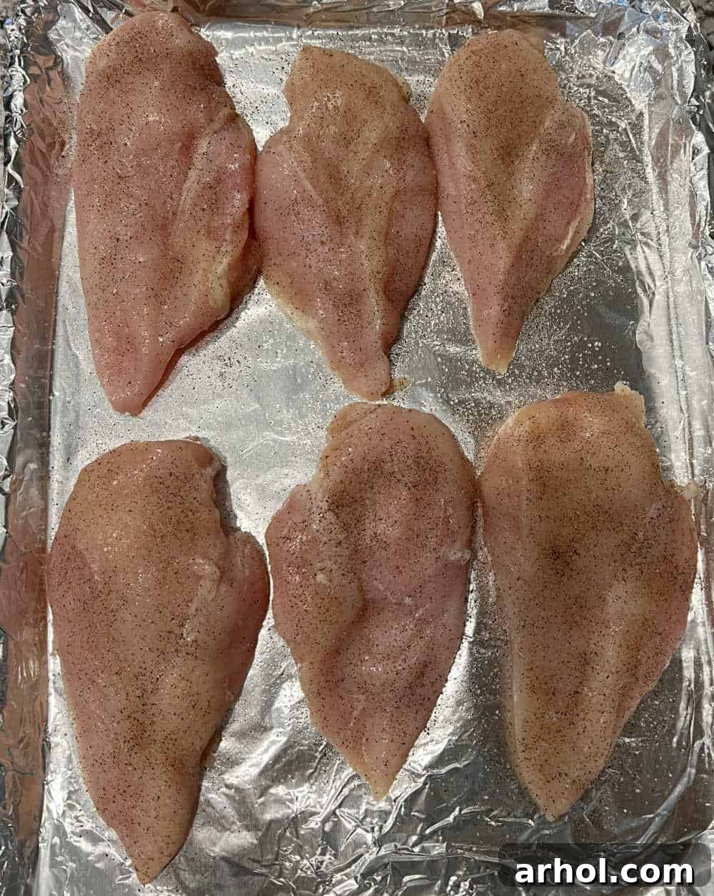 Boneless, skinless chicken breasts neatly arranged and seasoned on a baking sheet, poised for the oven.
