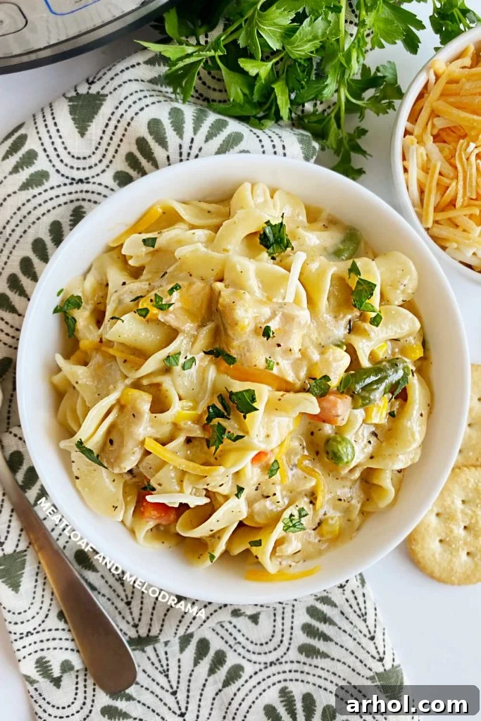 Instant Pot Tuna Noodle Casserole served in a white bowl, garnished with fresh parsley and extra shredded cheese, showcasing tender pasta, peas, and carrots in a creamy sauce.