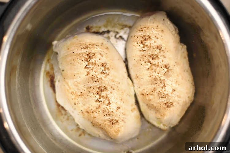 Two seasoned boneless, skinless chicken breasts browning in an Instant Pot on the SAUTE setting.