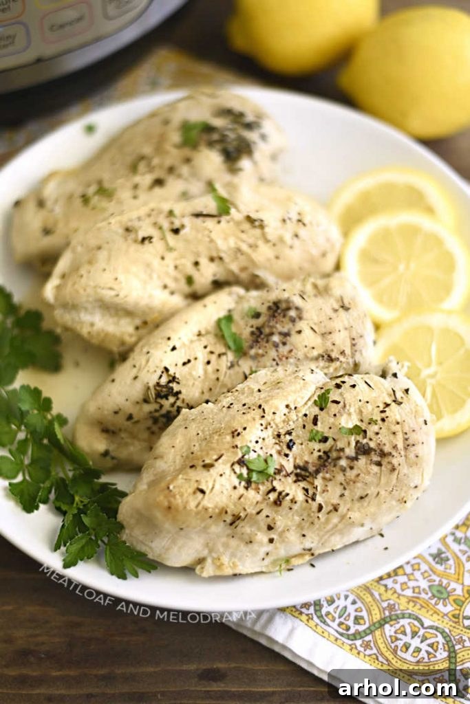 Cooked Instant Pot chicken breasts displayed on a serving platter with lemon wedges and fresh parsley.