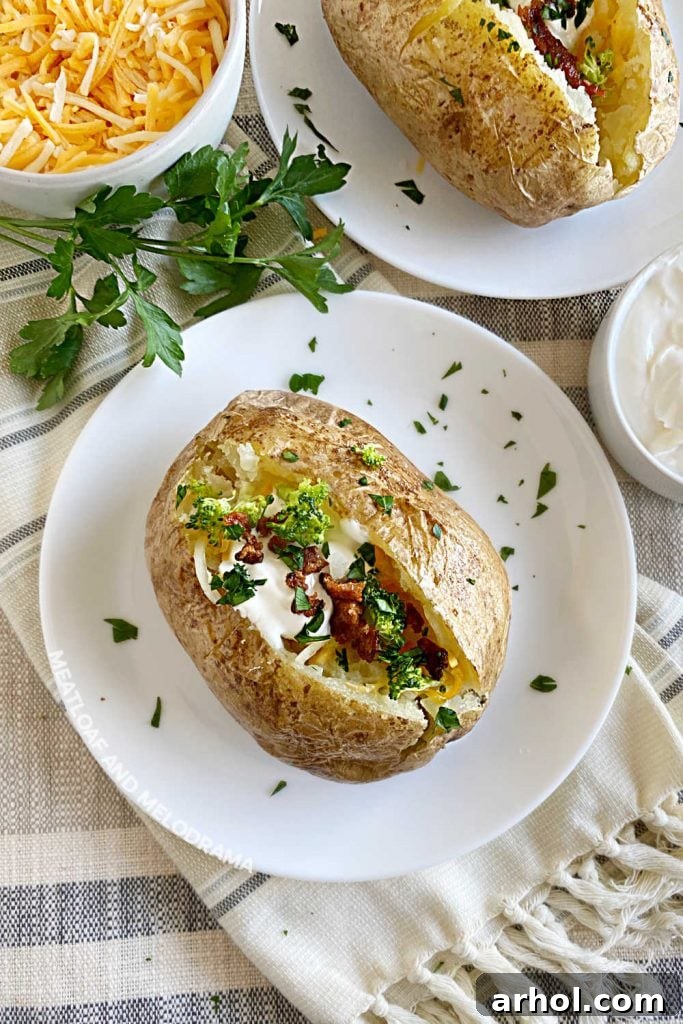 Two perfectly baked potatoes topped with melted cheese and a dollop of sour cream on white plates.