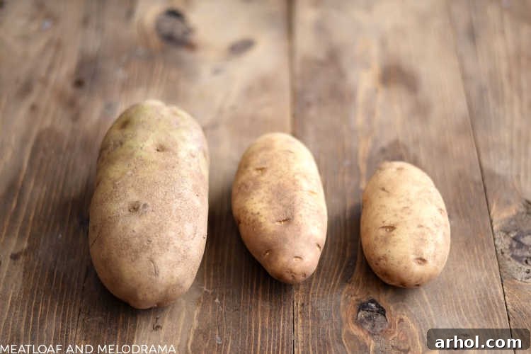 A visual comparison of large, medium, and small Russet potatoes neatly arranged on a rustic wooden board.