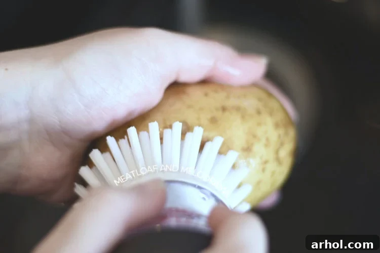 Close-up shot of a hand scrubbing a Russet potato under cold running water with a kitchen brush, emphasizing thorough cleaning.