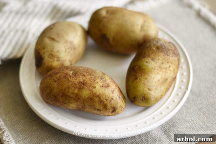 Three scrubbed and pricked Russet potatoes resting on a white microwave-safe plate, ready for cooking.