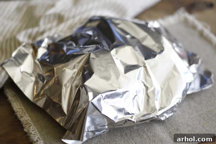 Freshly microwaved potatoes resting on a plate, covered with aluminum foil to trap steam and continue cooking.