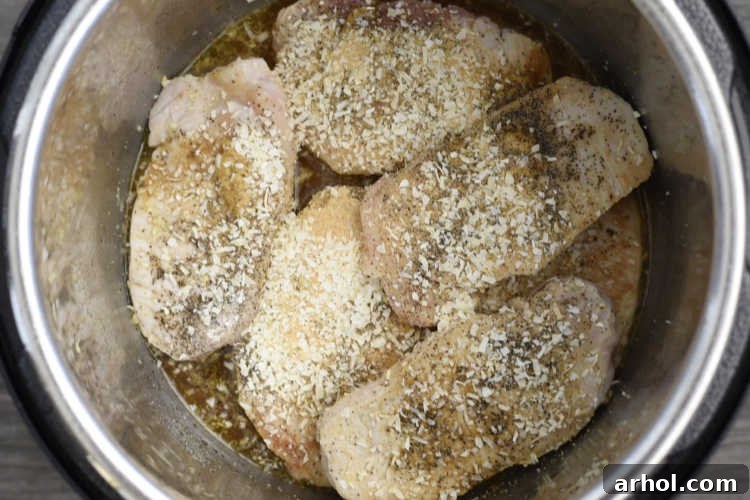 Boneless pork chops seasoned and nestled in the Instant Pot with broth, ready for pressure cooking to create tender results.