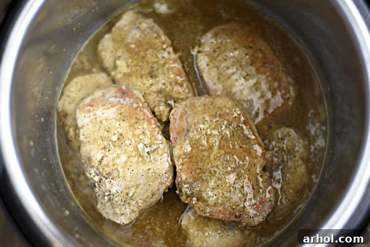 Cooked Instant Pot pork chops immersed in rich, bubbling gravy within the pressure cooker, signaling a delicious meal.