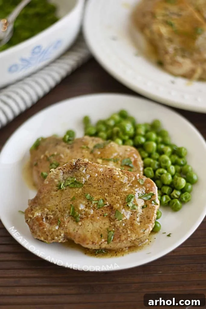 Two boneless Instant Pot pork chops generously smothered in savory homemade gravy, served with a side of green peas on a white plate.