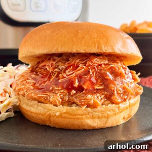 A pulled Instant Pot BBQ chicken sandwich on a brioche bun, served with a side of coleslaw on a black plate.