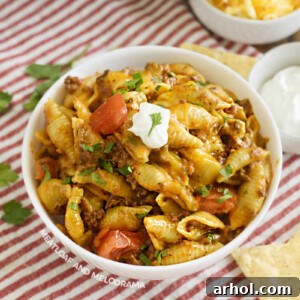 A bowl of creamy Instant Pot Taco Pasta garnished with a dollop of sour cream and diced tomatoes.