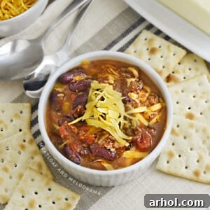 A white bowl filled with Instant Pot Chili, garnished with shredded cheese and a side of saltine crackers.
