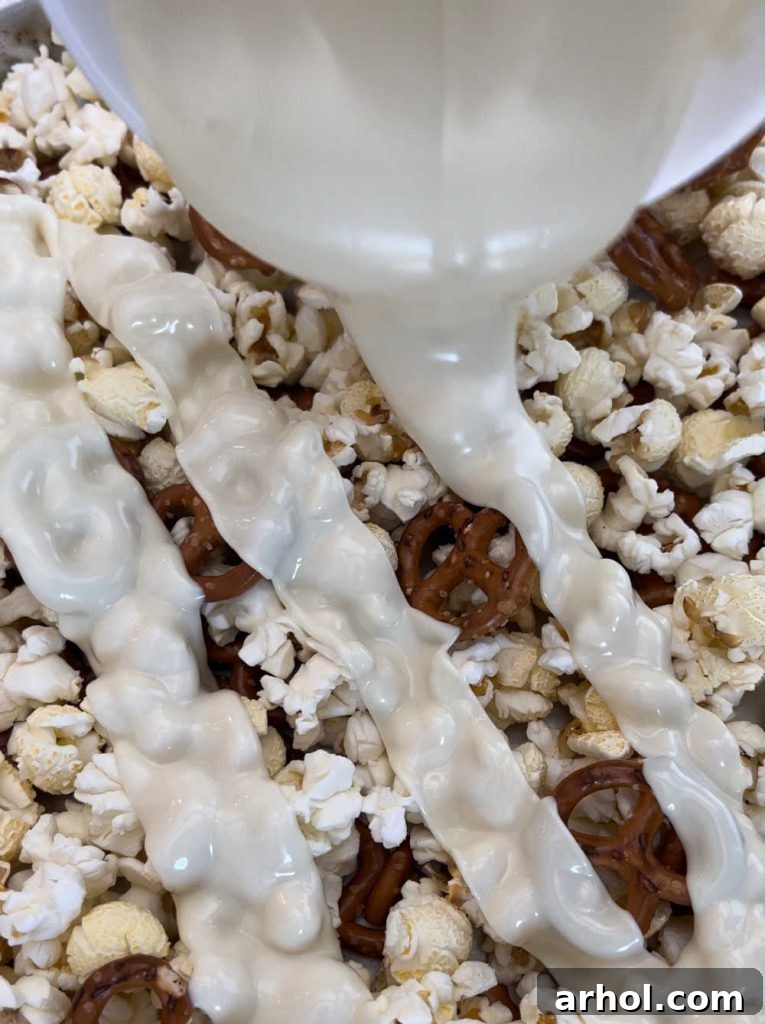 Stars and Stripes Popcorn Treat 4 Melted white chocolate drizzled over popcorn kernels on a baking sheet, ready for mixing