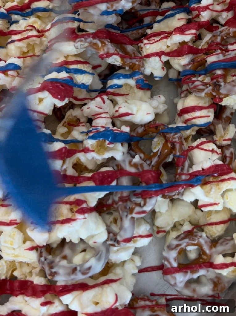 Stars and Stripes Popcorn Treat 5 Red and blue candy coating being drizzled over a popcorn and pretzel mixture on a baking sheet