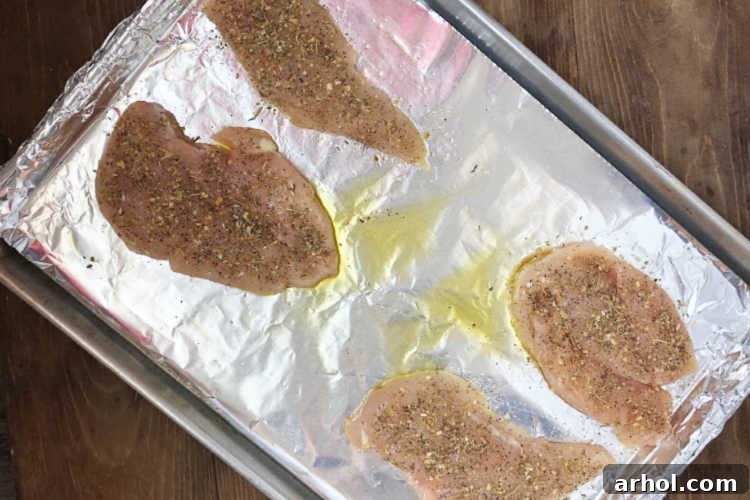 Thinly sliced chicken breasts seasoned and laid out on a large baking sheet, ready for vegetables.