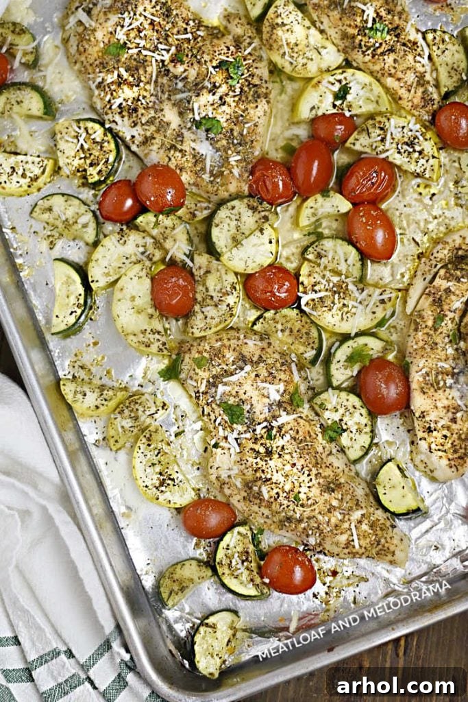 A perfectly baked sheet pan dinner featuring golden-brown chicken breasts, softened zucchini and yellow squash, and glistening grape tomatoes, fresh out of the oven.
