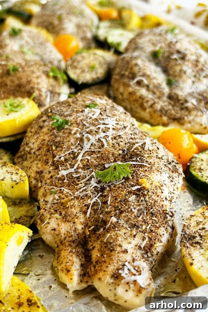 A close-up of seasoned baked chicken breast with perfectly roasted zucchini and yellow squash, glistening with olive oil on a sheet pan.