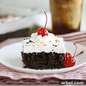 A perfectly sliced piece of chocolate root beer float cake, topped with a generous swirl of cool whip frosting and a vibrant maraschino cherry.