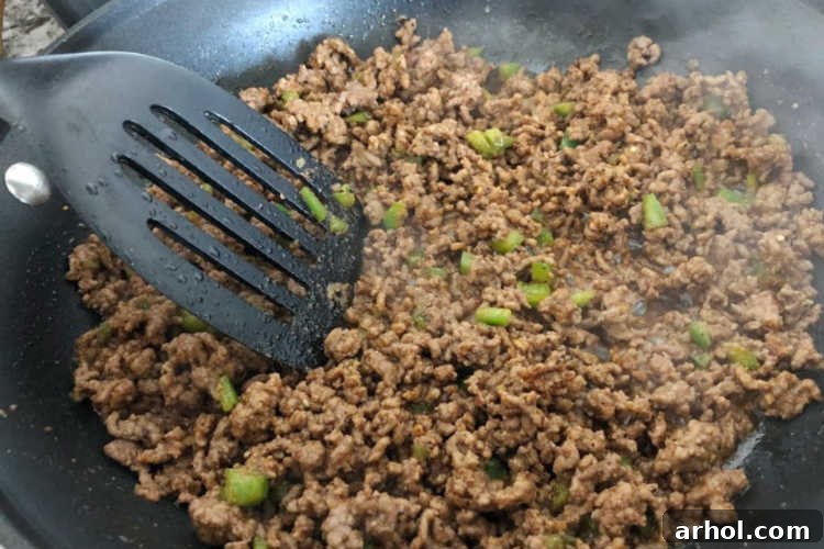 Sautéing ground beef with finely chopped jalapeño peppers in a large skillet.