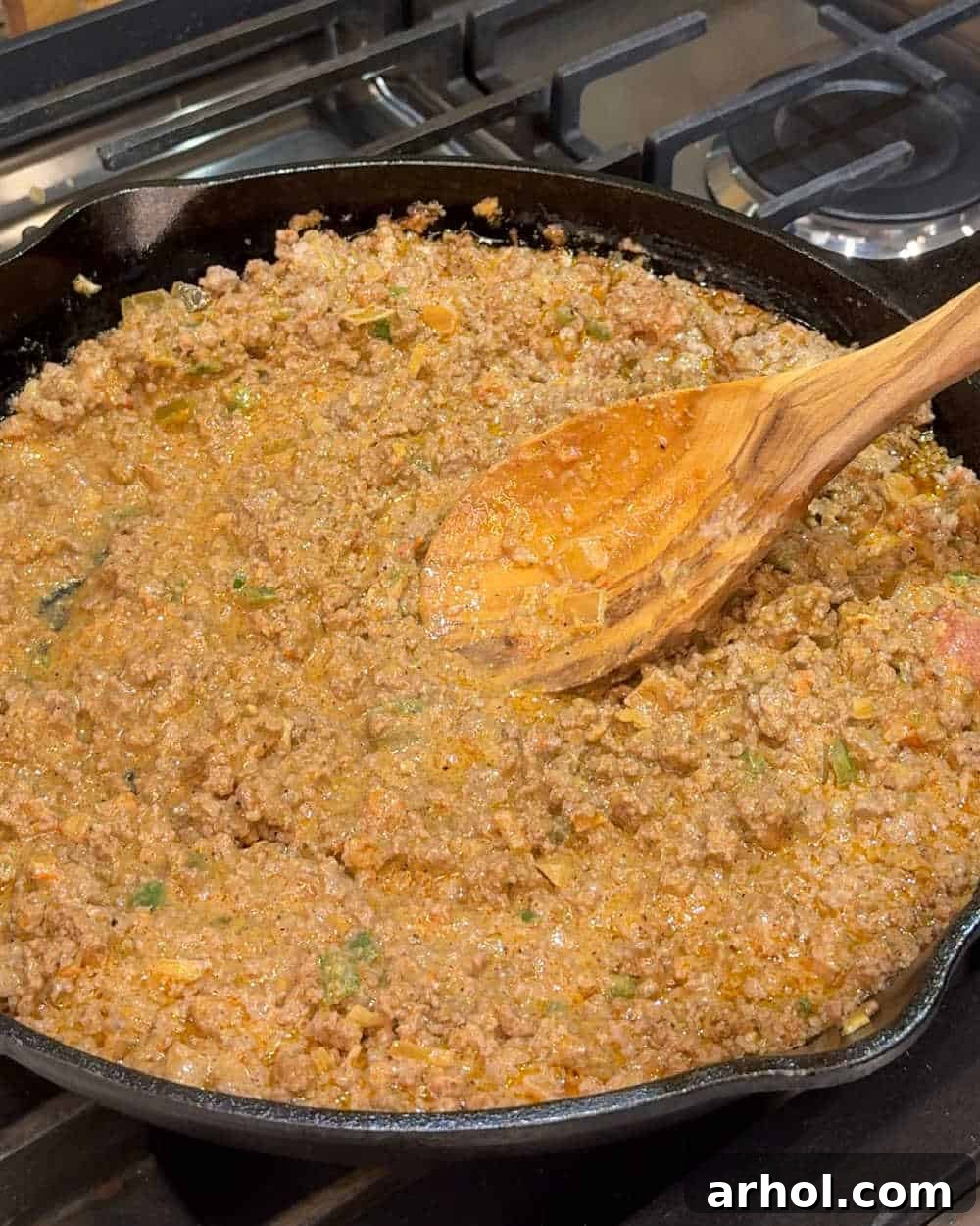 Stirring the seasoned ground beef mixture with sour cream and salsa using a wooden spoon.