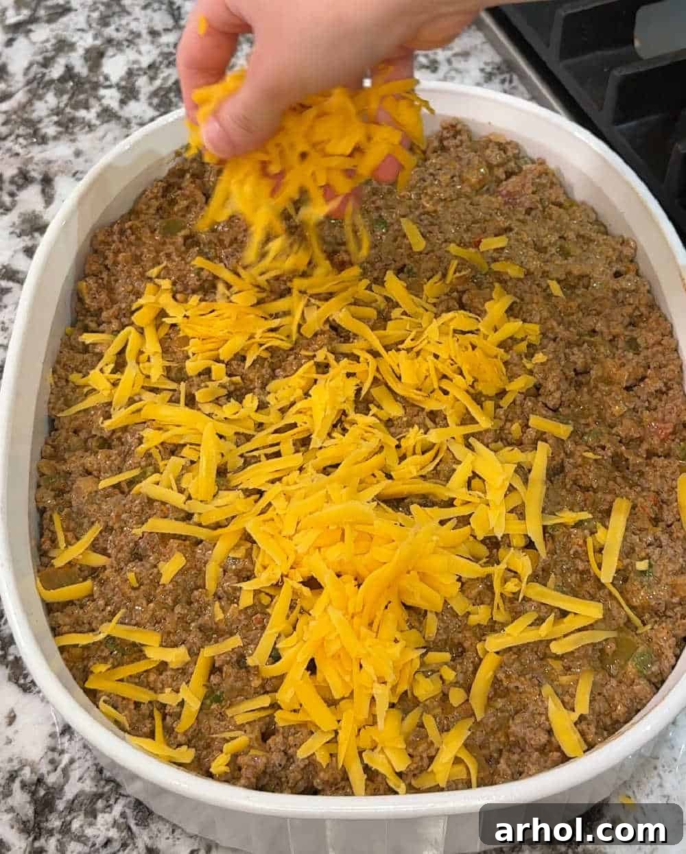 Sprinkling shredded cheese evenly over the ground beef mixture in the casserole dish.