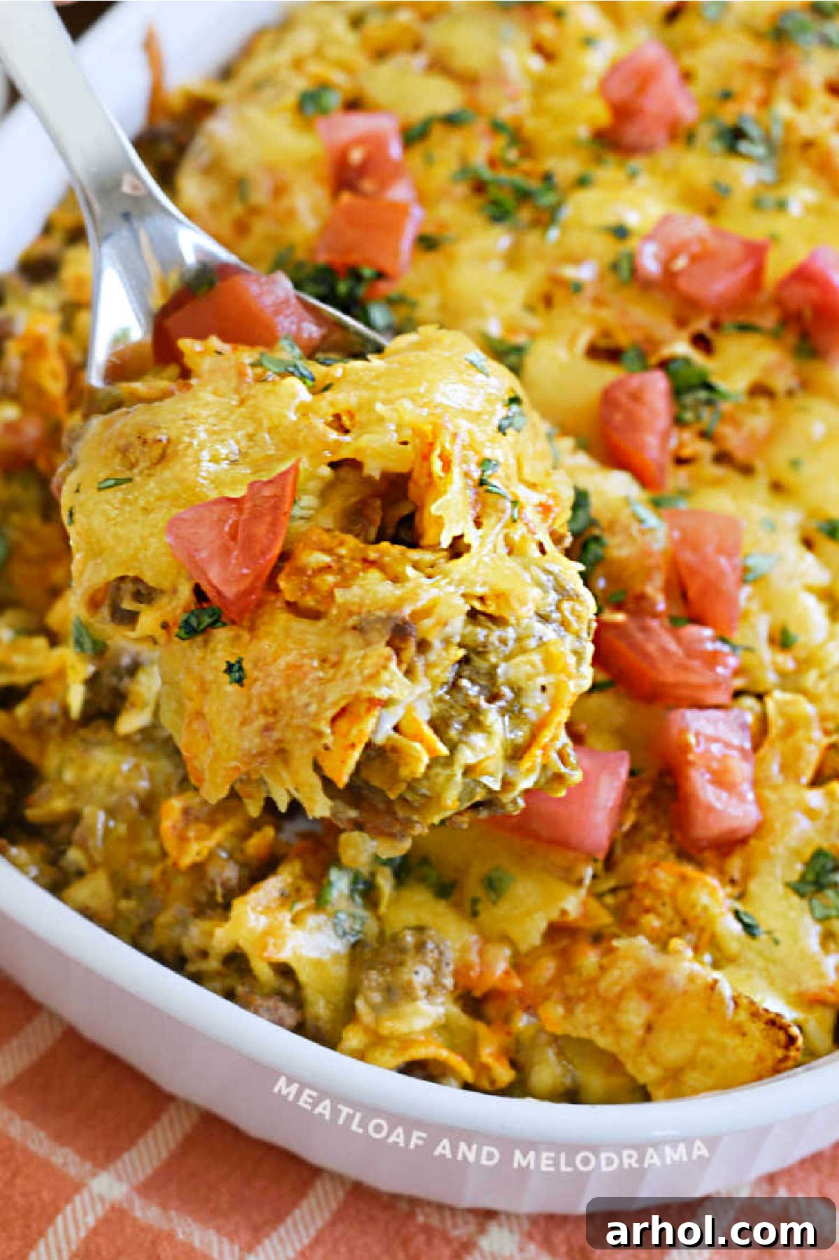 A spoonful of Dorito Casserole with ground beef, melted cheese, and diced tomatoes, lifted from the baking dish.